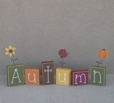 the word autumn spelled out with wooden blocks and flowers on top of each block in front of a wall