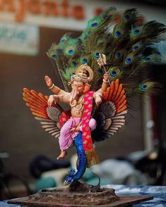 a figurine of a man with peacock feathers on his head and arms outstretched