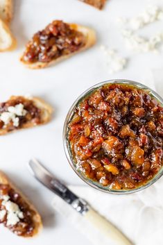 a glass jar filled with food sitting on top of a white table next to bread