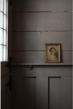 a framed portrait is on the ledge of a door in an empty room with wood paneling