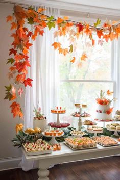 a table topped with lots of food next to a window covered in fall colored leaves