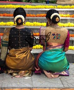 two women sitting on the steps in front of flowers and garlands, both wearing sari