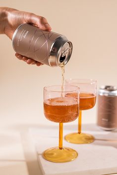 a person pours some liquid into two glasses with gold rims on a white surface