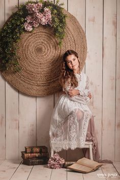 a woman sitting on a chair in front of a wall hanging with flowers and books