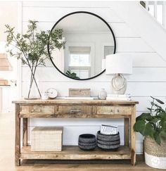 a wooden table topped with a round mirror next to a lamp and a vase filled with flowers