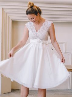 a woman in a white dress is standing near a fireplace with her foot on the table