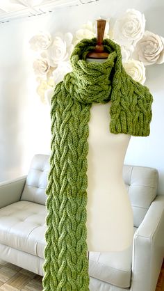 a green knitted scarf on a mannequin with white flowers in the background