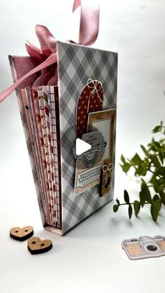 an open gift bag sitting next to some buttons and a plant with pink ribbon on it