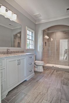 a large bathroom with gray tile floors and white cabinets, along with a walk in shower