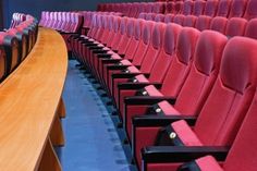 an empty auditorium with rows of red seats and wooden table in front of the audience