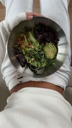 a woman is holding a metal bowl full of vegetables and avocado on her stomach