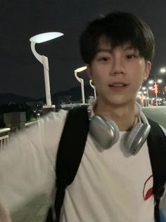 a young man with headphones on standing in front of a street light at night