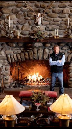 a man standing in front of a fire place with candles on the mantle and deer heads above it