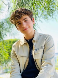 a young man sitting under a tree with his hands on his hips and looking at the camera