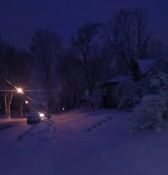 a snowy street at night with cars parked on the side and trees covered in snow