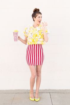 a woman in a striped skirt holding two popcorns while standing next to a white wall