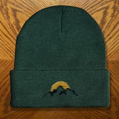 a green beanie with a bird embroidered on the front and yellow circle at the bottom