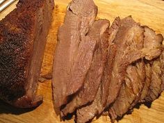 sliced beef on a cutting board with tongs next to it and another piece of meat in the background