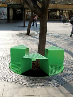 a green bench sitting under a tree on a sidewalk