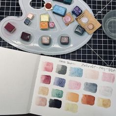 an artist's palette and watercolors on a table next to a notebook