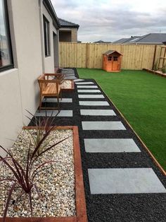 a small backyard with grass, gravel and wooden benches on the side of the house