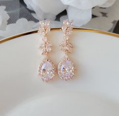 two pairs of pink and white diamond earrings on a plate with flowers in the background