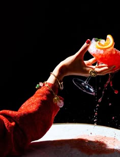 a woman's hand holding a wine glass with an orange slice in it and splashing water