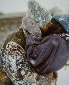 two people are hugging in the snow with one holding his head to her chest, while the other is wearing a blue and gray hat