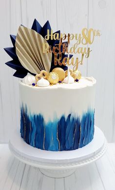 a birthday cake decorated with blue and white icing, gold decorations and a fan