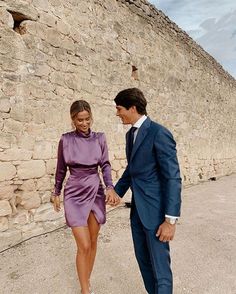 a man in a suit and tie walking next to a woman in a purple dress