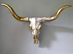 a bull's skull mounted on the side of a wall with gold colored horns