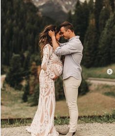 a man and woman standing next to each other in front of some mountains with trees