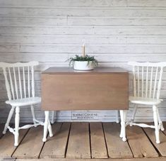 two white chairs sitting on top of a wooden floor next to a table with a potted plant