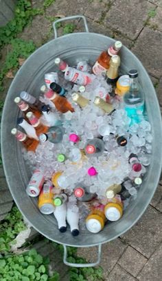 a metal bucket filled with lots of bottles and ice on top of a brick walkway