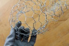 a hand holding up a wire ball on top of a wooden floor next to a pair of gloves