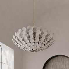 a white chandelier hanging from the ceiling in a room with brick wall and round mirror