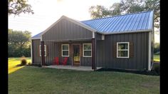 a small gray house with a blue roof and red chairs in the front yard area