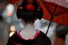 a geisha woman with an umbrella in her hand and wearing a red hat on top