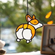 a stained glass dog hanging from a chain on a window sill in front of a tree