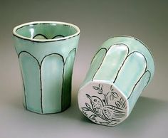 two green cups with designs on them sitting next to each other in front of a gray background