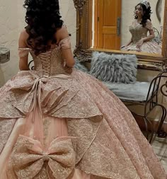 a woman in a ball gown is looking at herself in the mirror while wearing a large bow