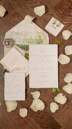 the wedding stationery is laid out on top of the wooden table with rose petals