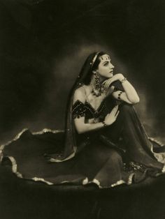 an old black and white photo of a woman with her hands on her knees, sitting down