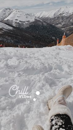 someone's feet in the snow on top of a hill with mountains in the background