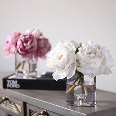 two vases filled with white and pink flowers sitting on top of a wooden table