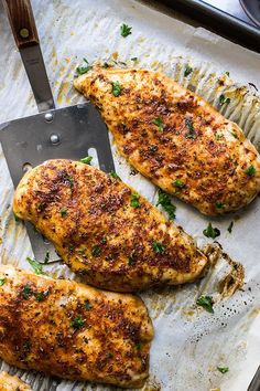 two pieces of chicken sitting on top of a pan next to a spatula