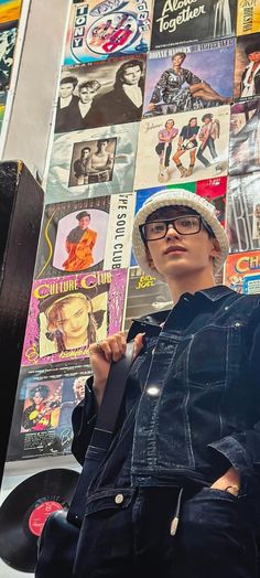 a mannequin wearing glasses and a hat in front of a wall covered with vinyl records