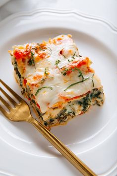 a piece of lasagna on a white plate with a gold fork next to it