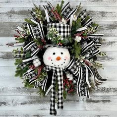 a snowman wreath with black and white plaid ribbon, evergreens and berries on it