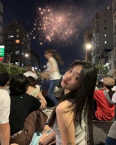 a woman looking up at the sky with fireworks in the air and people sitting on the ground